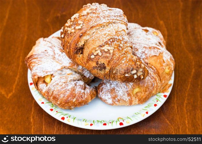 three fresh italian croissants filled by vanilla and chocolate creams on wooden table