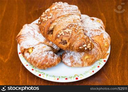three fresh italian croissants filled by vanilla and chocolate creams on wooden table