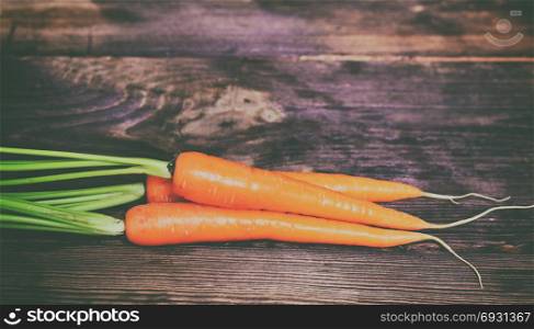 Three fresh orange carrots on a brown wooden table, close up