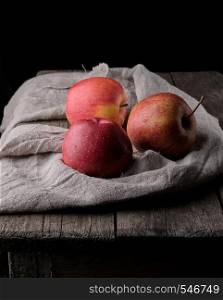 three fresh red apples lay on gray linen napkin, dark background