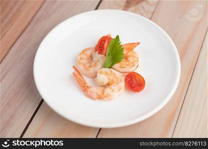 Three fresh shrimp and half tomatoes in a white plate on a wooden.