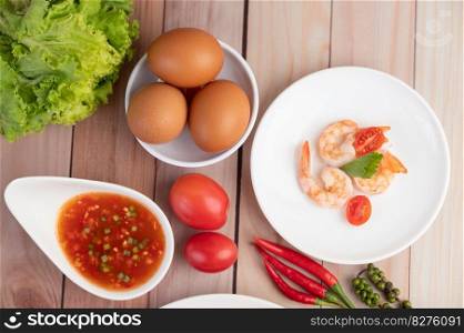 Three fresh shrimp, eggs, chili, sauce and half tomatoes in a white plate on a wooden.