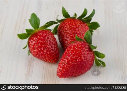 Three fresh strawberries on white wooden background.