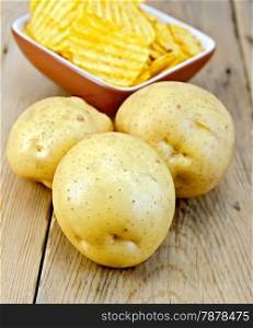 Three fresh yellow potato tuber, potato chips in a clay bowl on a wooden boards background