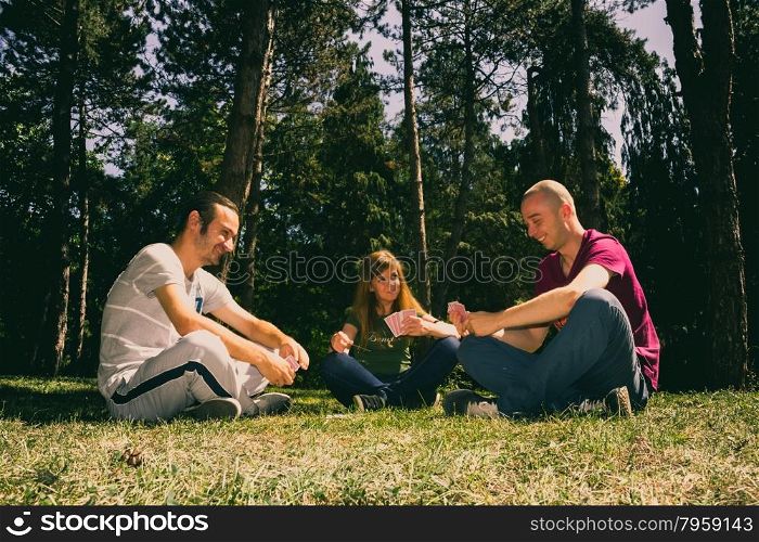 Three friends having fun by playing cards in the forest