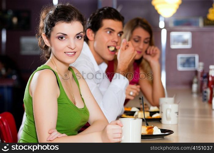 Three friends in a restaurant or diner eating cheesecake and drinking coffee