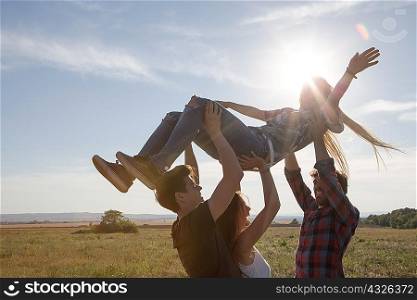 Three friends lifting young woman above their heads