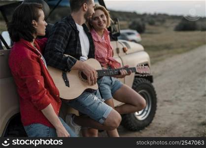 three friends playing guitar while traveling by car