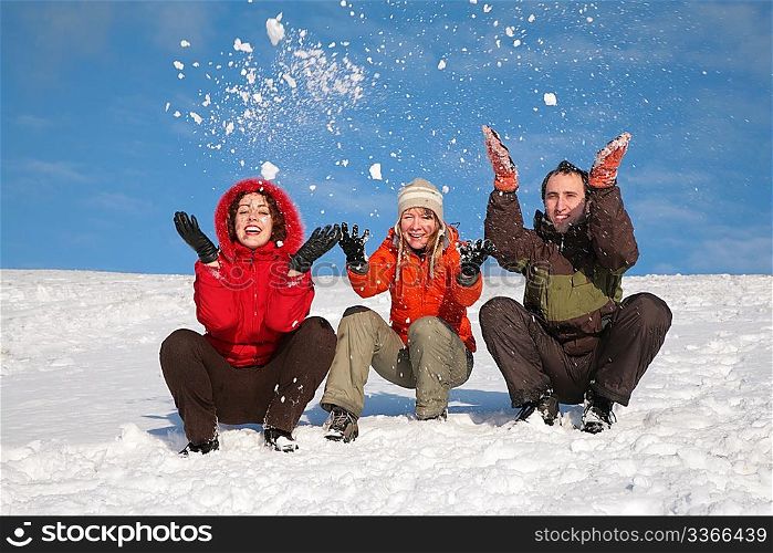 three friends sit on snow and throw snows