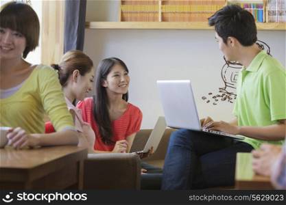 Three friends sitting in coffee shop, using laptop and talking