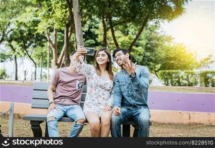 Three friends sitting on a bench taking a selfie, Three teenage friends sitting on a bench taking selfies. Gathering of three happy friends taking a selfie sitting on a bench