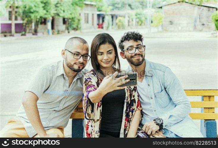 Three friends taking a selfie on a park bench, Three smiling friends sitting on a bench taking a selfie. Front view of three happy friends taking a selfie while sitting on a bench