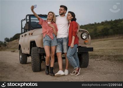 three friends taking selfie with smartphone while traveling by car