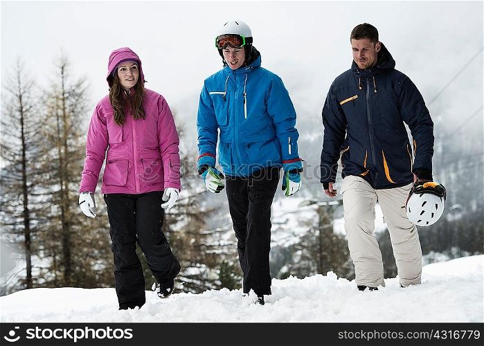 Three friends wearing skiwear walking in snow
