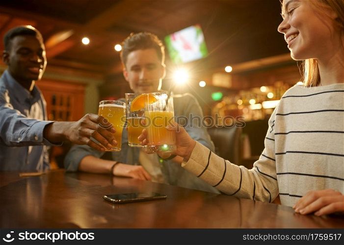 Three friends with alcohol beverages having fun at the table in bar. Group of people relax in pub, night lifestyle, friendship, event celebration. Friends with alcohol beverages having fun in bar