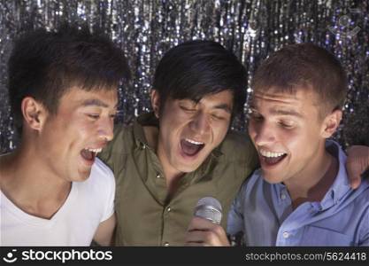 Three friends with arm around each other holding a microphone and singing together at karaoke