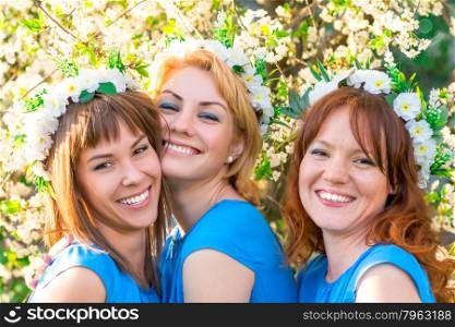 three friends with wreaths on the head near the blossoming cherry in the park