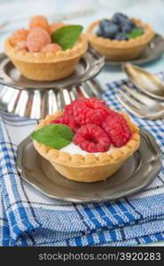 Three fruit tartlets with red and yellow raspberries and blueberries on a vintage plate closeup