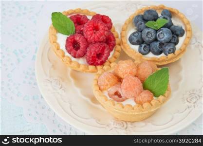 Three fruit tartlets with red and yellow raspberries and blueberries on a vintage plate closeup