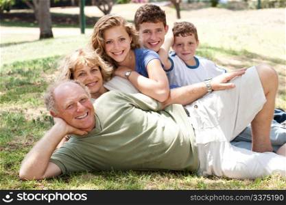 Three generation Caucasian family lying on green grass in the park smiling.
