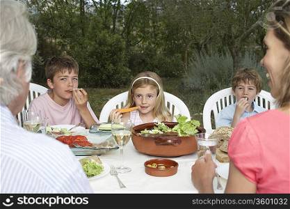 Three-generation family with three children (6-11) sitting at table in garden