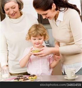 Three generations women around cupcake little girl tasting cookies