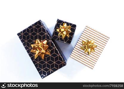 Three gift boxes are black-gold with a geometric pattern and a gold bow and black with a white and gold shiny lid and a gold bow. Isolate on a white background. View from above.