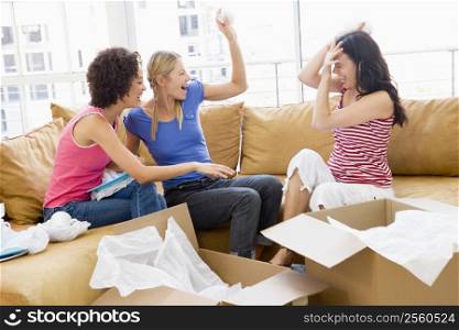 Three girl friends playfully unpacking boxes in new home smiling