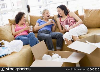 Three girl friends relaxing with coffee by boxes in new home smiling