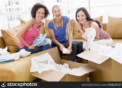 Three girl friends unpacking boxes in new home smiling
