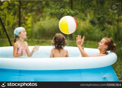 Three girls are swimming in the blue pool and playing with ball. Girls in swimming pool