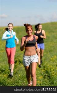 Three girls jogging downhill summer meadow and smiling