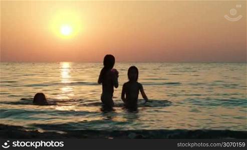 Three girls playing with ball in sea at sunset. Childrens activity and summer vacation