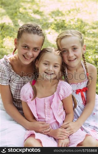 Three girls sit on the grass and smile. Three girls