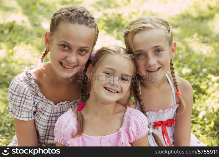 Three girls sit on the grass and smile. Three girls