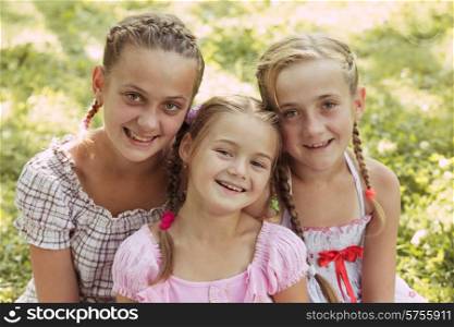 Three girls sit on the grass and smile. Three girls
