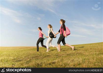 Three girls walking over a grass hill