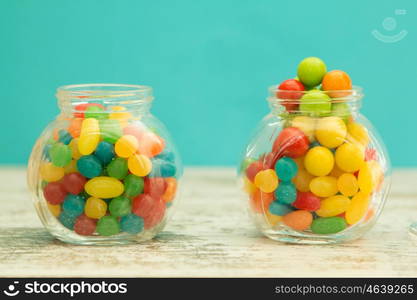 Three glass jars full of jellybeans on wooden table with blue background