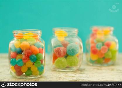 Three glass jars full of jellybeans on wooden table with blue background