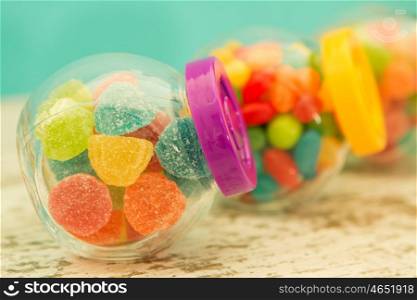 Three glass jars full of jellybeans on wooden table with blue background. Focus in the foreground