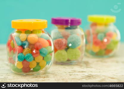 Three glass jars full of jellybeans on wooden table with blue background