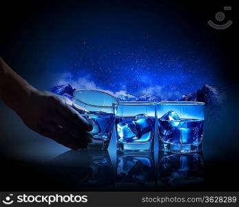 Three glasses of blue liquid with ice against mountain background