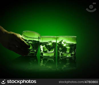 Three glasses of green absinth with ice cubes. Hand holding one of three glasses of green absinth with fume going out