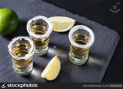 Three glasses of tequila with salt and lime on black background