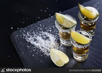 Three glasses of tequila with salt on the rim and lime on black background. Alcoholic cocktail. Mexican traditional drink. Three glasses of tequila with salt on the rim and lime