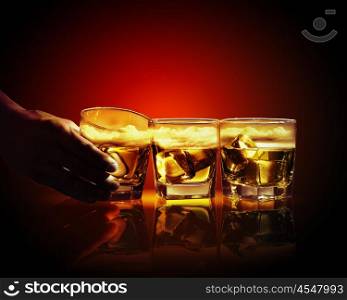 Three glasses of whiskey with ice cubes. Hand holding one of three glasses of whiskey with ice and sky illustration in