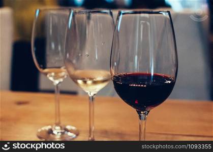three glasses with red and white wine, on wooden table, served for wine tasting event. Blurred background. Bar or restaurant interior, subdued light. Selective focus. Flm Grain effect