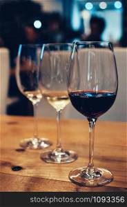 three glasses with red and white wine, on wooden table, served for wine tasting event. Selective focus, Film Grain effect. Blurred background. Bar or restaurant interior, subdued light