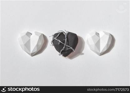Three gypsum hearts on a light grey background with shadows and copy space. One of them is black and wrapped twisted wire. Valentine&rsquo;s day greeting card.. Hearts set from plaster figures and one with wire.