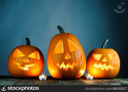 Three Halloween pumpkins head jack o lantern and candles on wooden table background. Halloween pumpkins and candles